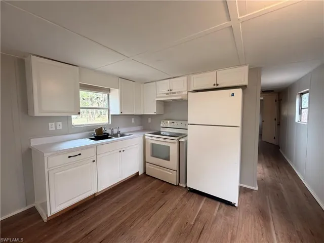 Kitchen with white cabinets, white appliances, light countertops, and healthy amount of natural light