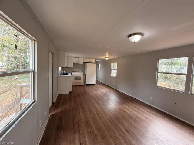 Kitchen featuring light countertops, white appliances, white cabinets, dark wood finished floors, and open floor plan