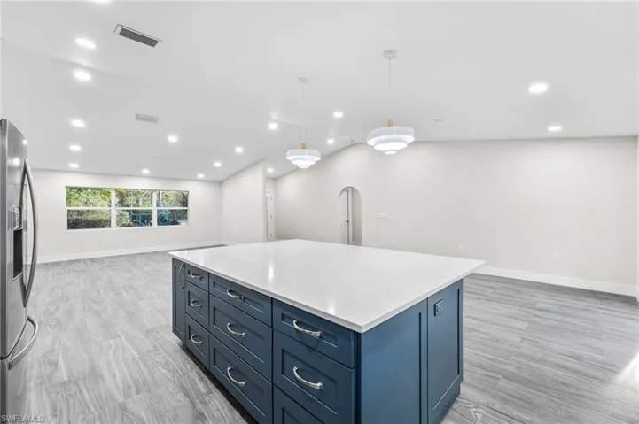 Kitchen featuring open floor plan, blue cabinetry, a center island, pendant lighting, and light wood-style floors