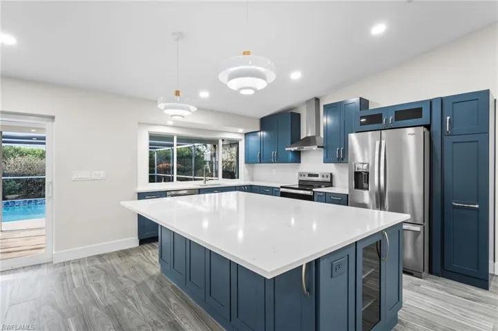 Kitchen with blue cabinetry, a kitchen island, pendant lighting, stainless steel appliances, and light wood finished floors