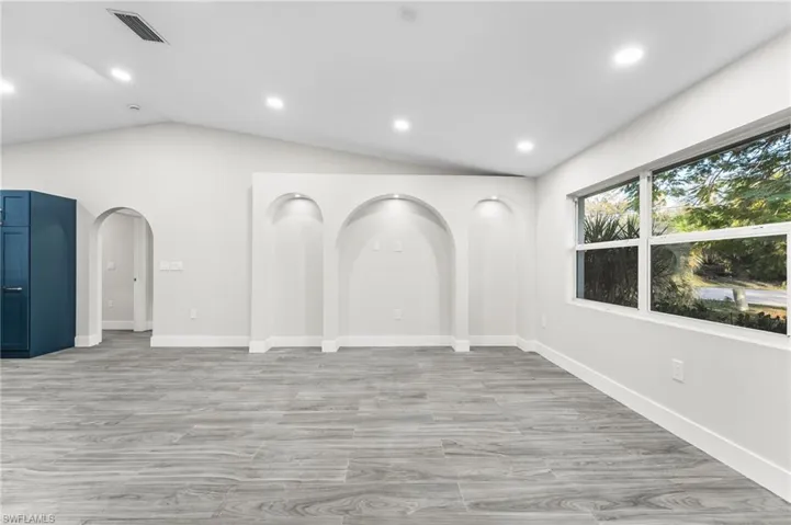 Living room featuring arched decorative areas, light wood-tile flooring, vaulted ceiling, and recessed lighting