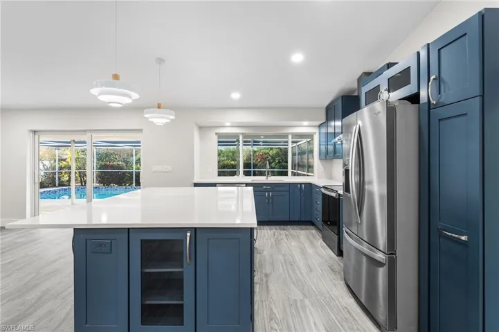 Kitchen with blue cabinetry, appliances with stainless steel finishes, decorative light fixtures, a kitchen island, and recessed lighting