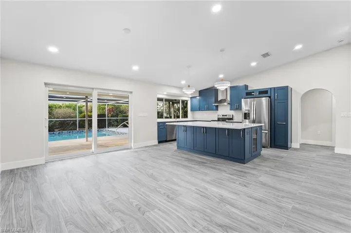 Kitchen with blue cabinetry, arched walkways, decorative light fixtures, a center island, and appliances with stainless steel finishes View out to the pool