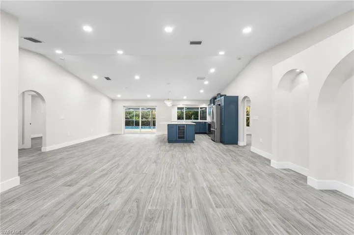 Huge living room with arched decorative areas, vaulted ceiling, recessed lighting, and light wood-tile flooring