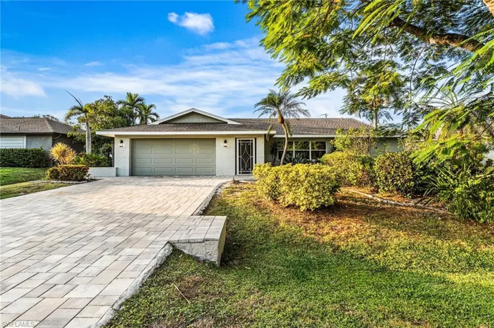 Ranch-style home with decorative driveway, stucco siding, a garage, and a front lawn with a beautiful Royal Ponciana tree in front yard.