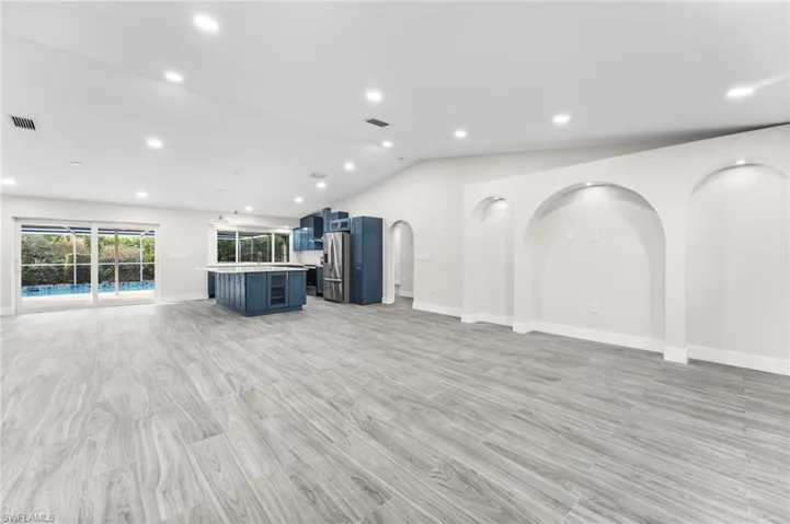 Living room with vaulted ceiling, recessed lighting, light wood-tile flooring, and arched entertainment or decorative areas.