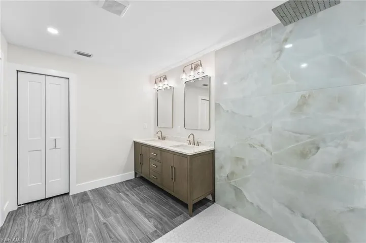 Full bath featuring double vanity, dark wood-style tile flooring, a closet, and recessed lighting
