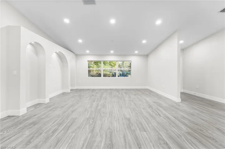 Living room with light wood-tile flooring, recessed lighting, and arched recessed areas