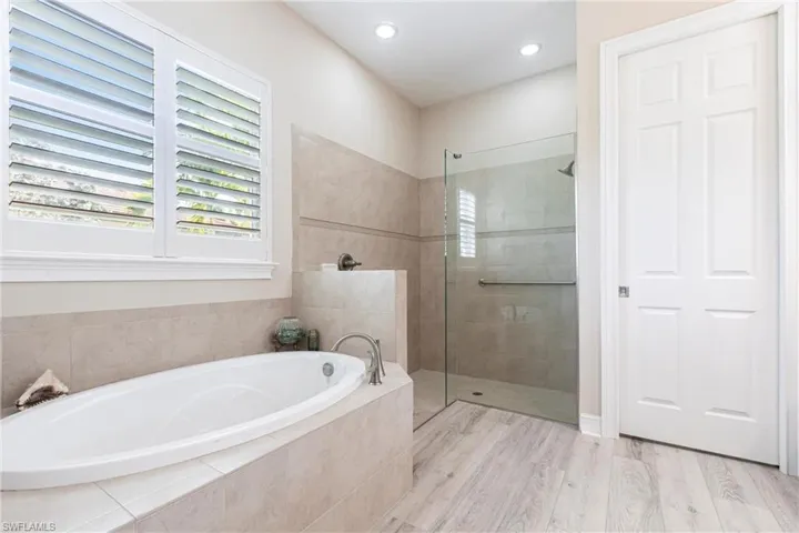 Bathroom with hardwood / wood-style flooring and separate shower and tub also featuring plantation shutters.