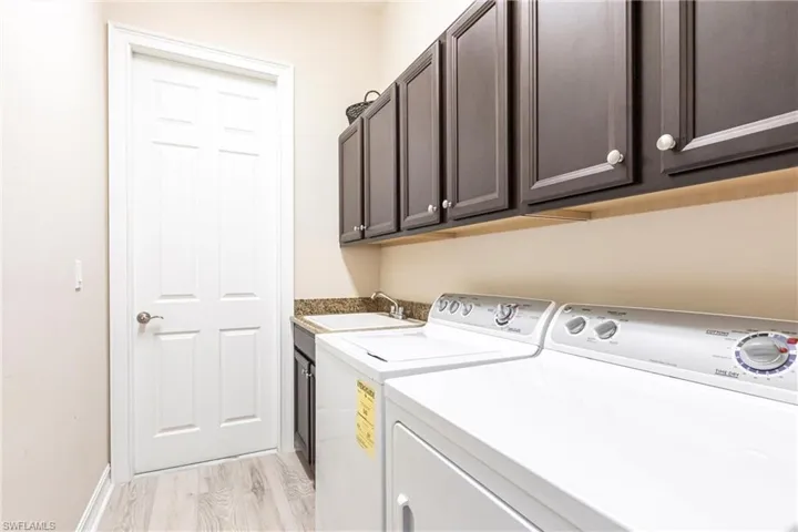 Laundry area with sink, washing machine and dryer, cabinets, and light wood-type flooring