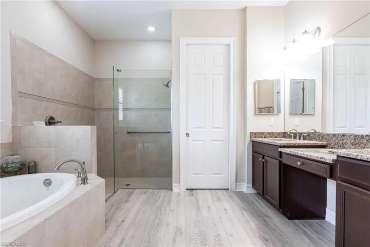Bathroom with vanity, dual sinks, independent shower and bath, separate room for commode and wood-type flooring