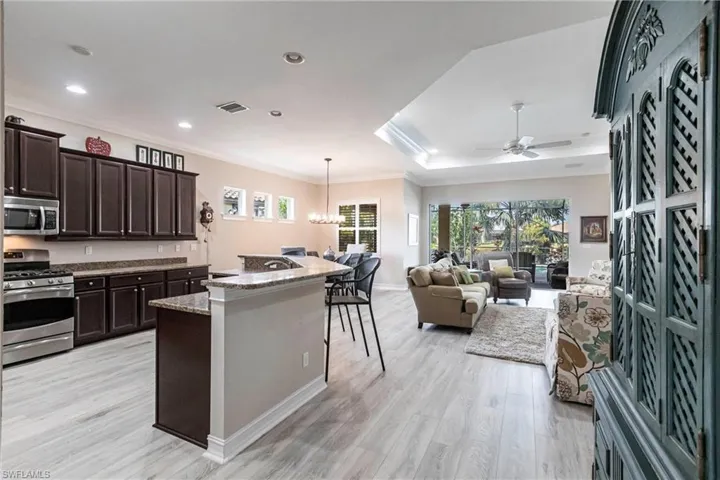 Kitchen featuring dark brown cabinetry, light hardwood / wood-style flooring, appliances with stainless steel finishes, ornamental molding, and pendant lighting