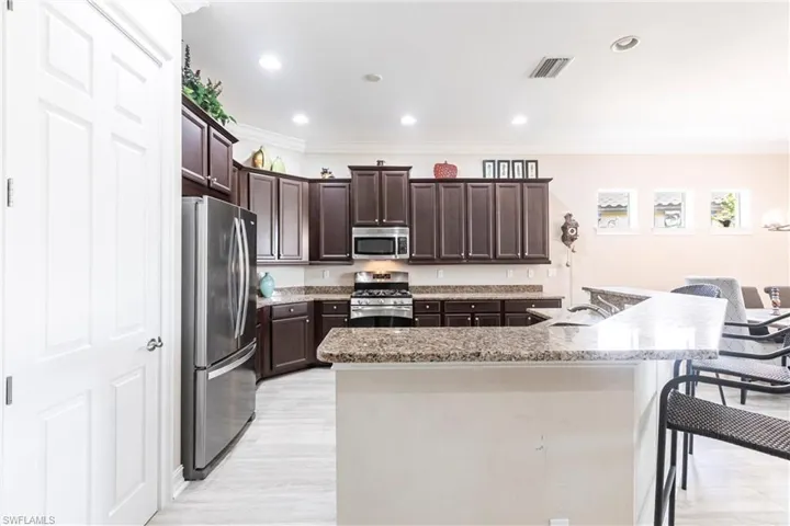 Kitchen with crown molding, dark brown cabinetry, appliances with stainless steel finishes, and a kitchen island with sink