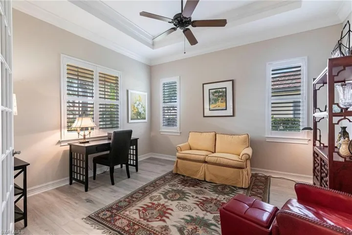 Office area with plantation shutters, ornamental molding, ceiling fan, light hardwood / wood-style floors, and a tray ceiling
