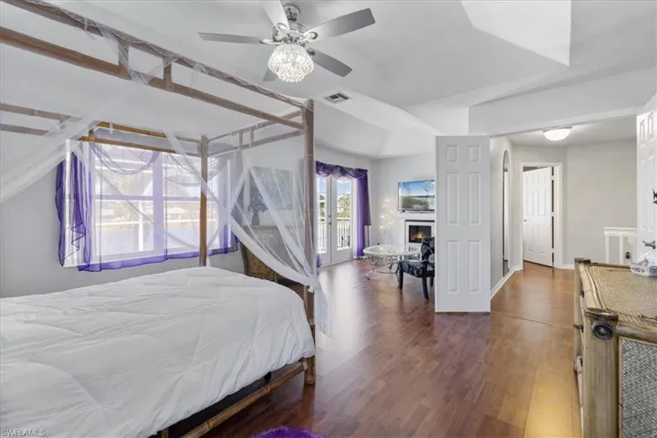 Bedroom with french doors, ceiling fan, a warm lit fireplace, visible vents, and wood finished floors