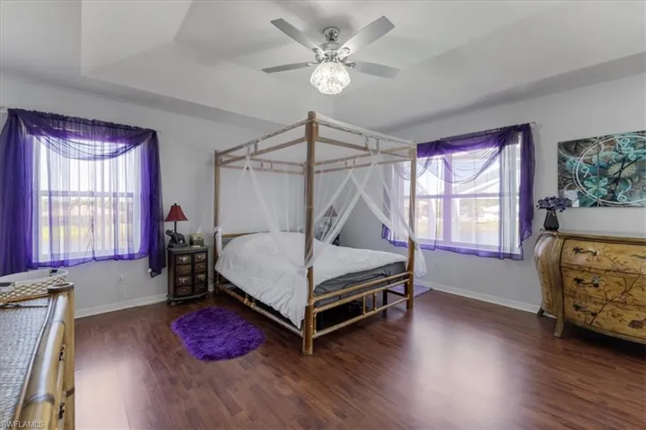 Bedroom with a ceiling fan, a tray ceiling, baseboards, and wood finished floors
