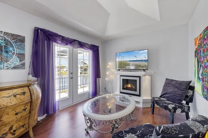 Living area featuring french doors, a warm lit fireplace, a raised ceiling, and wood finished floors