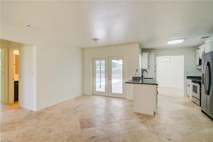 Kitchen with stainless steel appliances, light stone finish flooring, white cabinets, and french doors
