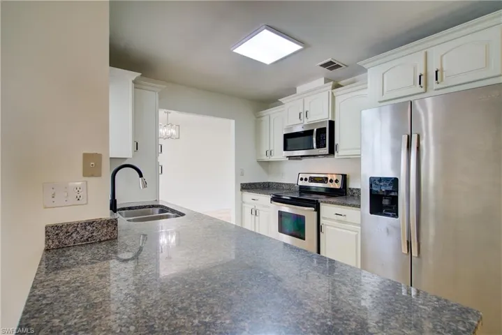 Kitchen featuring appliances with stainless steel finishes, white cabinets, a chandelier, dark stone countertops, and a peninsula