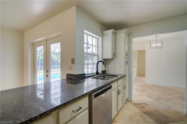 Kitchen with stainless steel dishwasher, a chandelier, plenty of natural light, and dark stone counters
