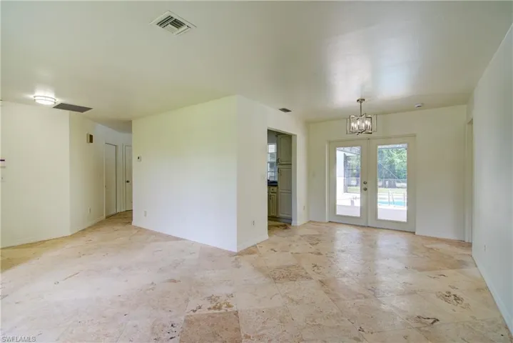 Empty room featuring a chandelier, french doors, and light stone finish floors
