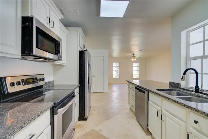 Kitchen with appliances with stainless steel finishes, dark stone countertops, white cabinetry, and a ceiling fan