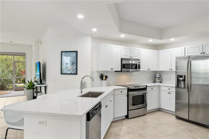 Kitchen with kitchen peninsula, white cabinetry, sink, and appliances with stainless steel finishes