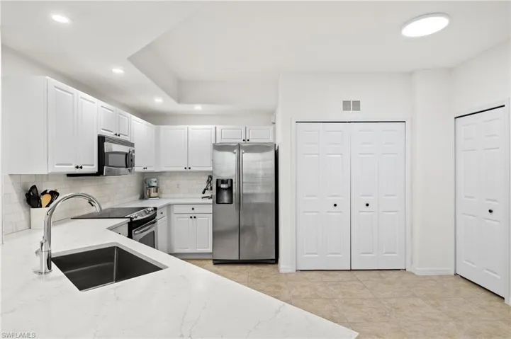 Kitchen featuring white cabinets, stainless steel appliances, sink, and light stone counters