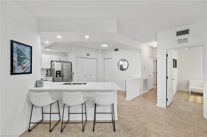 Kitchen featuring sink, kitchen peninsula, a kitchen breakfast bar, white cabinets, and stainless steel fridge