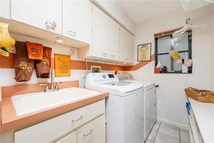 Clothes washing area featuring separate washer and dryer, cabinets, sink, and light tile patterned flooring