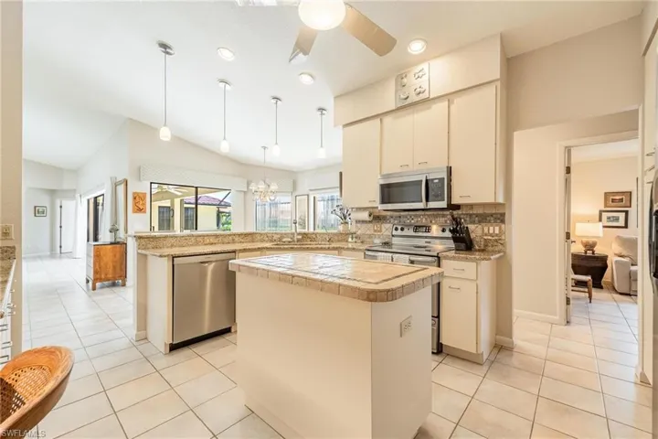 Kitchen with hanging light fixtures, ceiling fan with notable chandelier, stainless steel appliances, lofted ceiling, and a center island