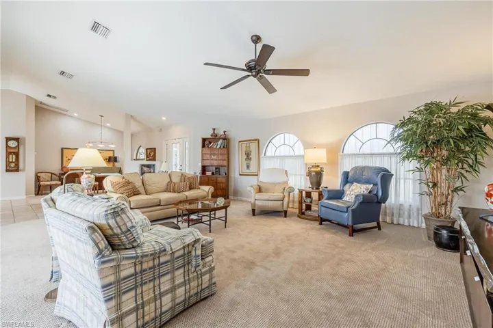 Living room with vaulted ceiling, ceiling fan, and light colored carpet