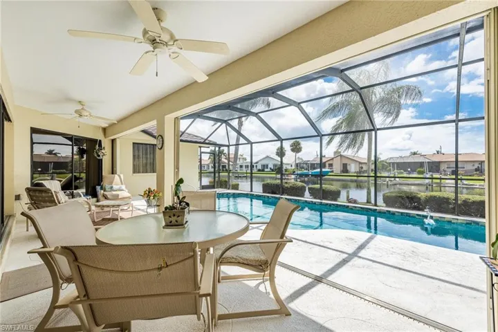 View of swimming pool featuring ceiling fan, a water view, glass enclosure, and a patio area