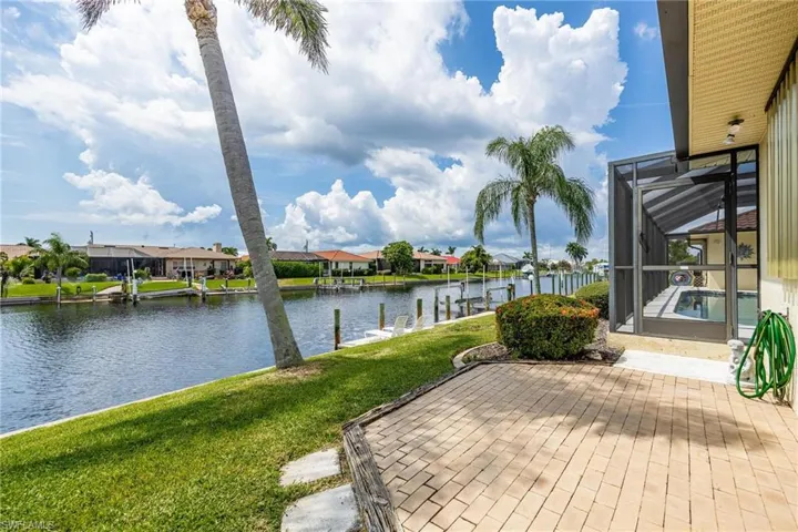 Wooden deck with glass enclosure, a water view, and a lawn