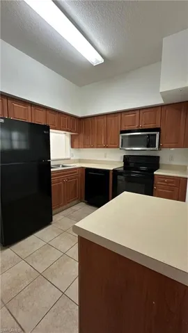 Kitchen with light countertops, a textured ceiling, light tile patterned floors, and black appliances