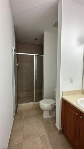 Full bathroom featuring a textured ceiling, a stall shower, toilet, visible vents, and vanity