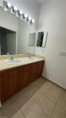 Bathroom featuring baseboards, tile patterned flooring, a sink, and double vanity