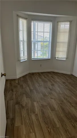 Empty room featuring a wealth of natural light, dark wood-type flooring, and baseboards