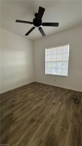 Unfurnished room featuring baseboards, a ceiling fan, and dark wood-style floors