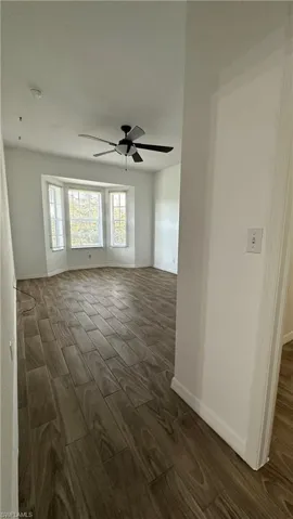 Empty room with wood tiled floor, a ceiling fan, and baseboards