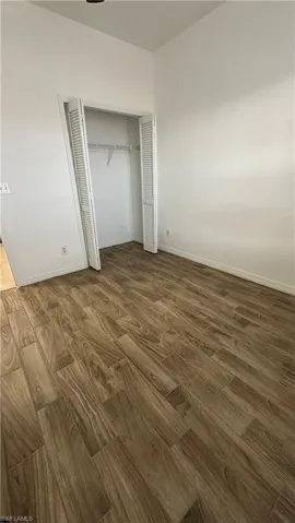 Unfurnished bedroom featuring a closet, baseboards, and dark wood-style flooring