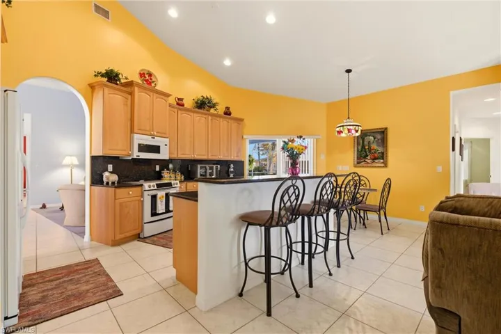 Kitchen with arched walkways, a breakfast bar, white appliances, and light tile patterned floors