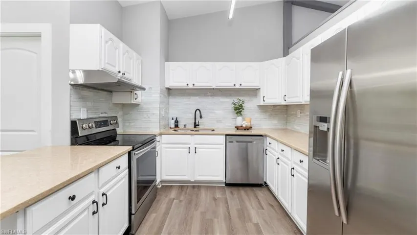 Kitchen featuring appliances with stainless steel finishes, white cabinets, light wood-style floors, light stone counters, and backsplash