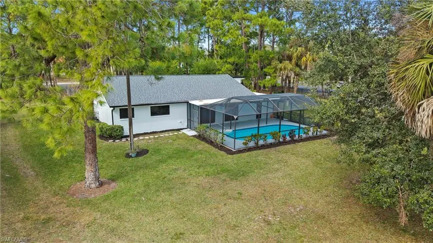 Rear view of house featuring a sunroom, glass enclosure, an outdoor pool, a yard, and roof with shingles
