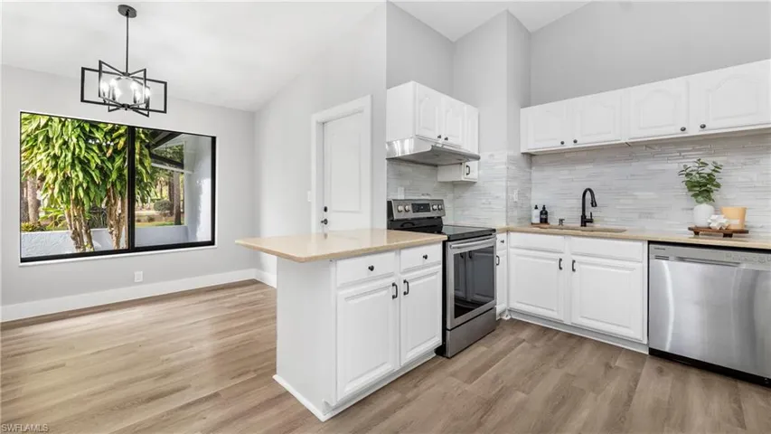Kitchen with stainless steel appliances, light stone countertops, pendant lighting, vaulted ceiling, and light wood-style floors