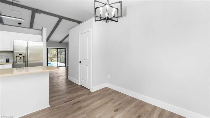Kitchen with high end fridge, white cabinetry, light wood-type flooring, light stone counters, and hanging light fixtures