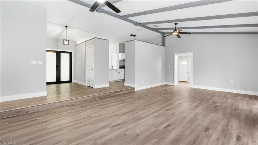 Unfurnished living room featuring beamed ceiling, french doors, light wood-type flooring, a ceiling fan, and high vaulted ceiling