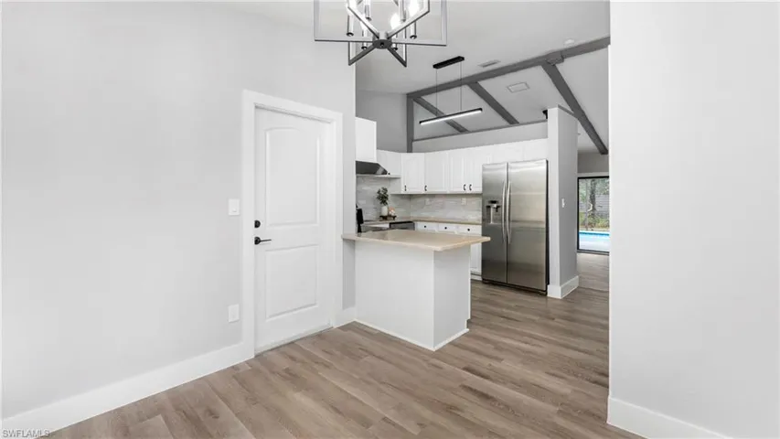 Kitchen with stainless steel fridge, light countertops, white cabinetry, high vaulted ceiling, and a peninsula
