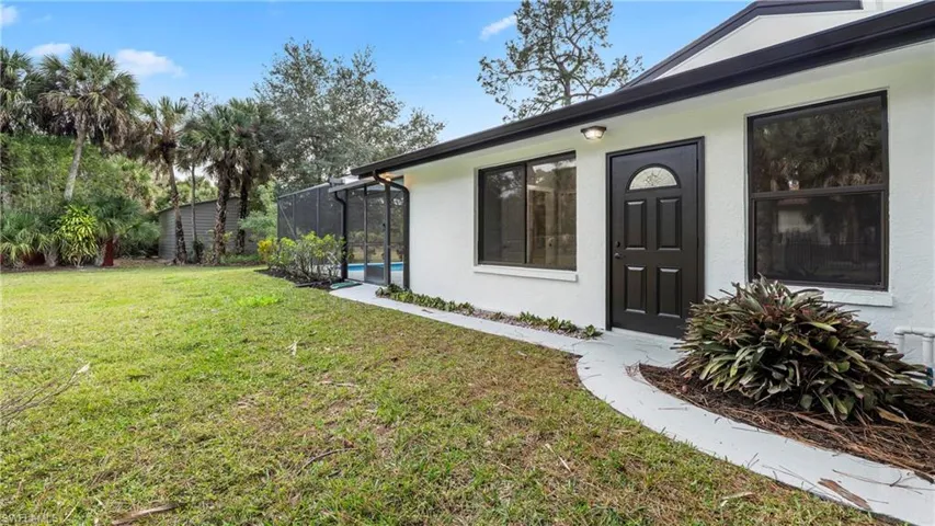 View of exterior entry featuring stucco siding, a lawn, and a sunroom
