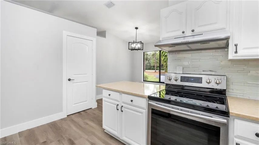 Kitchen with stainless steel electric range oven, white cabinetry, under cabinet range hood, decorative backsplash, and decorative light fixtures